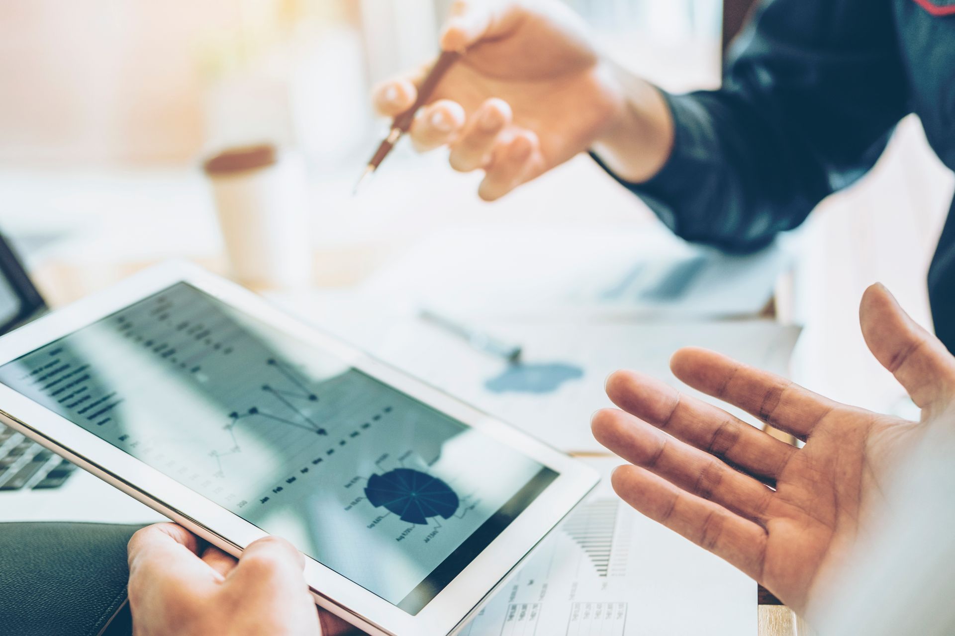 Hands discussing charts on a tablet and printed graphs at a desk