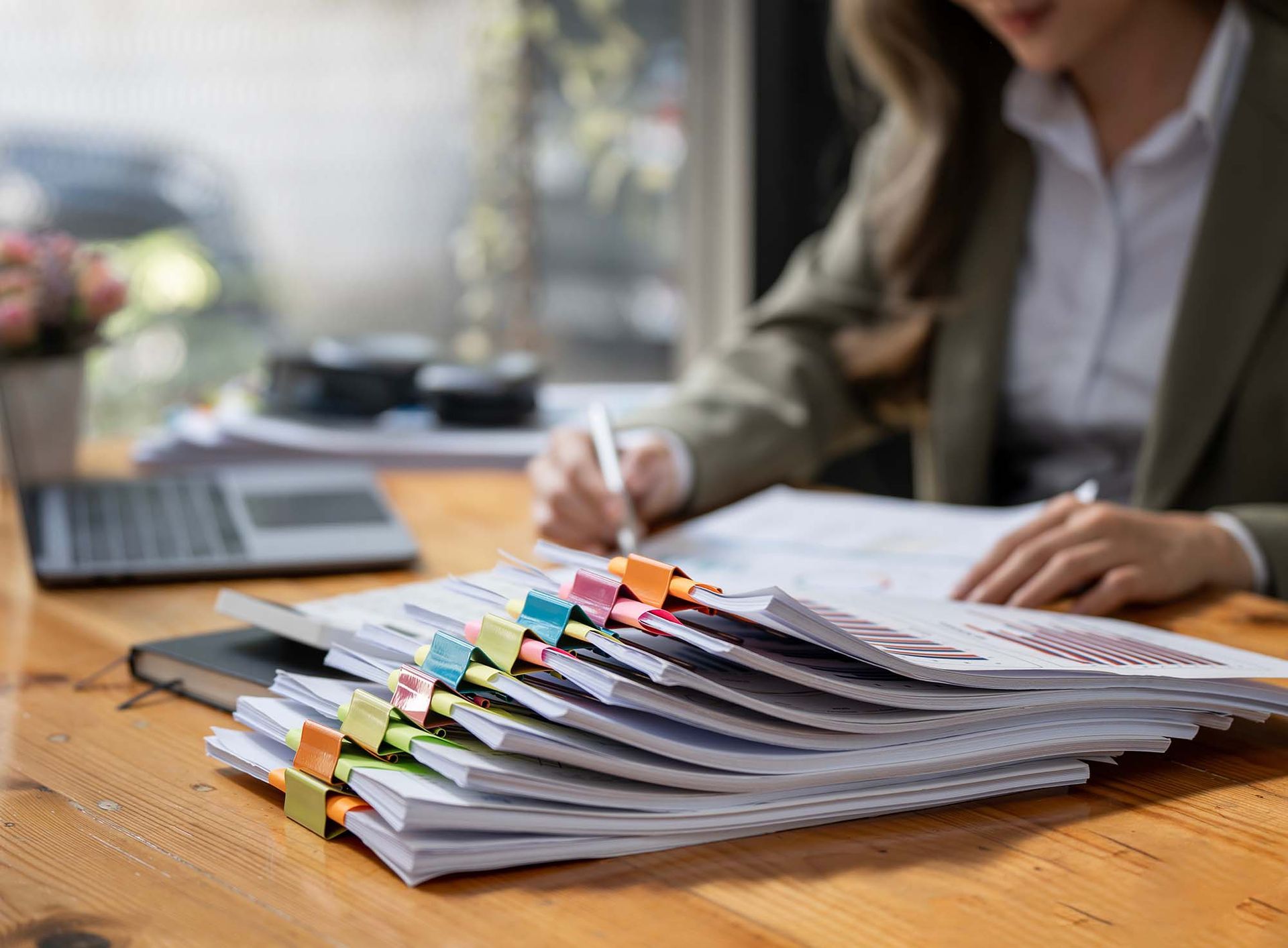 Person sorting a stack of colorful paper files at a wooden desk beside a laptop