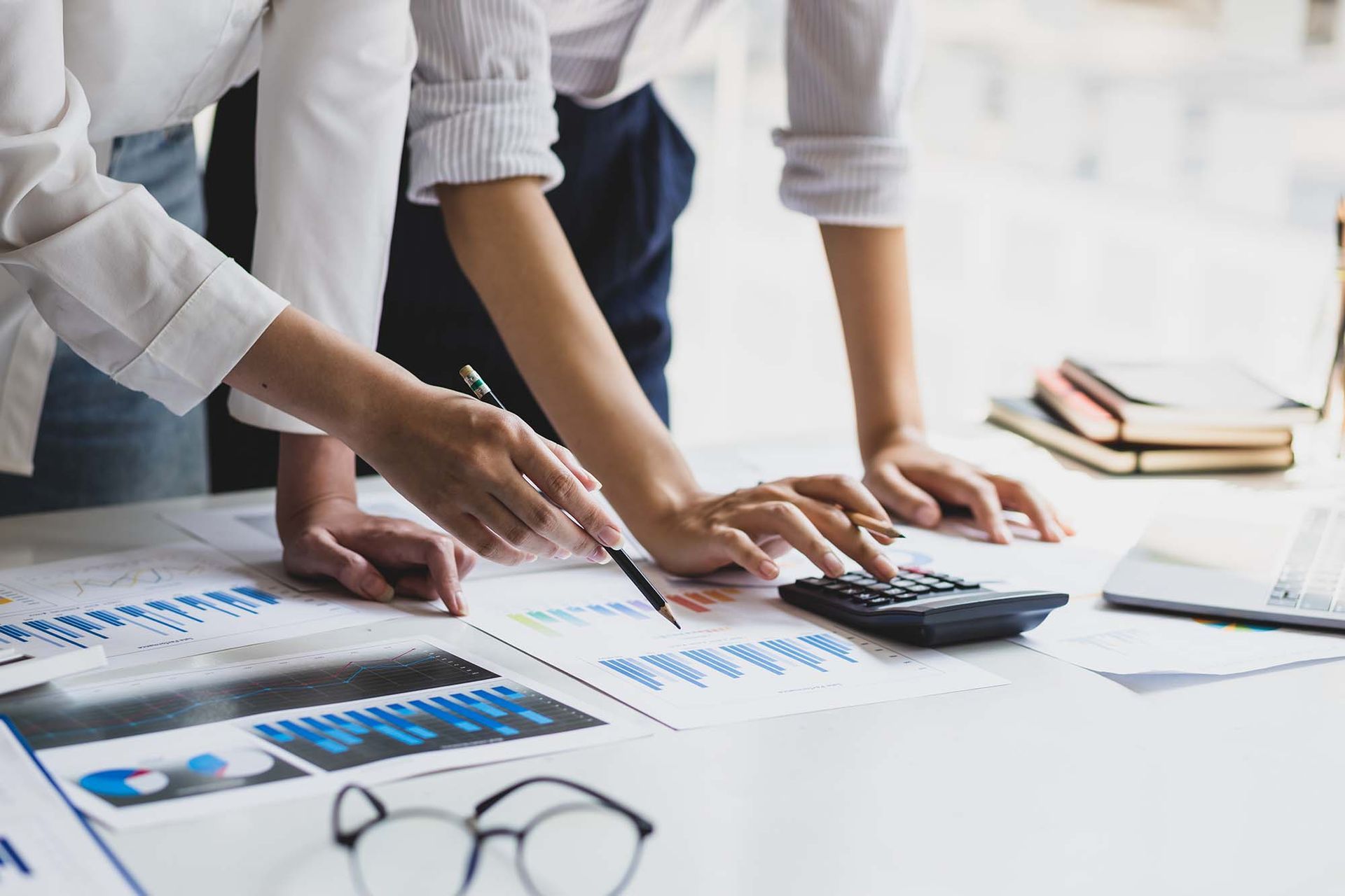 Three people reviewing charts and a calculator on a desk in a bright office