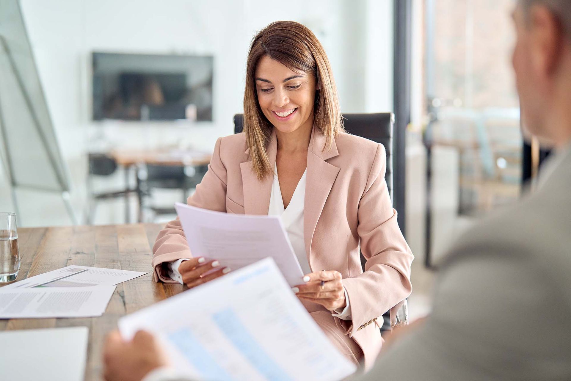 Woman in a pink blazer reviewing papers in a bright office meeting room