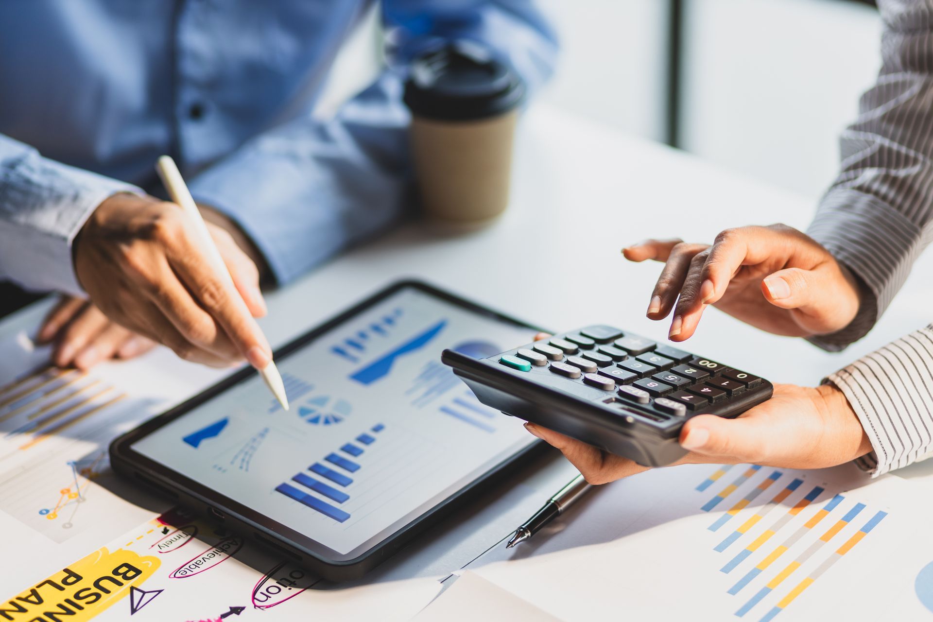 Hands using a tablet, calculator, and pen over printed charts during a financial review