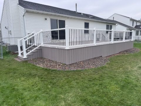 White house with raised wooden deck, white railing, and stairs overlooking a grassy yard.