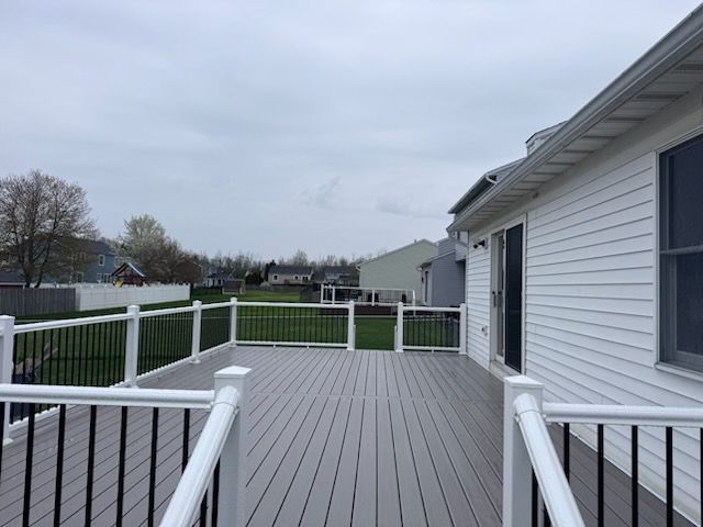 Back deck with gray flooring, white railing, and a view of a grassy backyard and neighboring houses