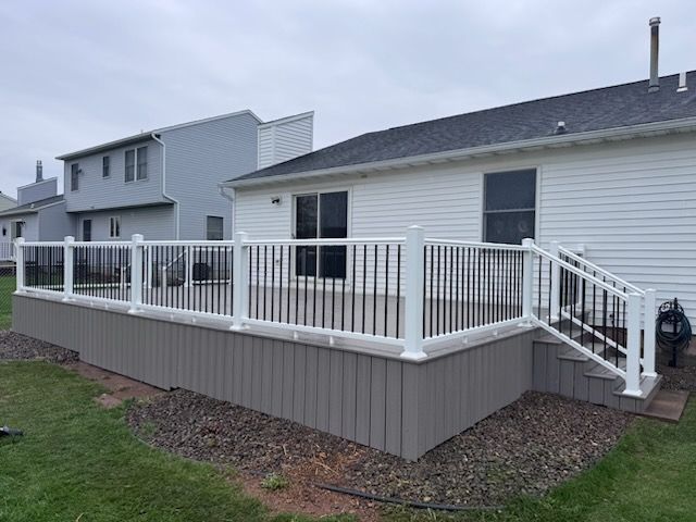 Raised gray deck with white railing attached to a house in a residential yard