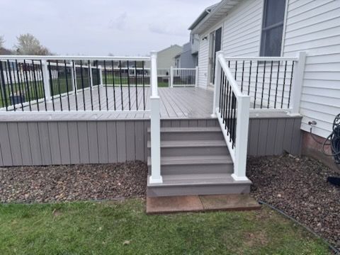 Backyard deck with gray stairs, white railings, and a concrete landing beside a house
