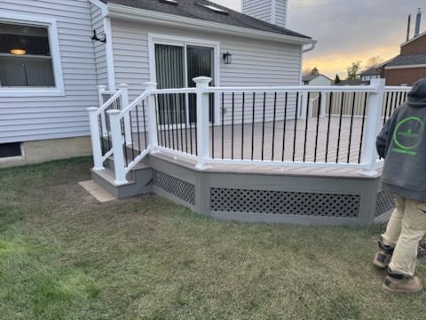 Back deck with white railings and lattice skirting beside a gray house; person walking at right
