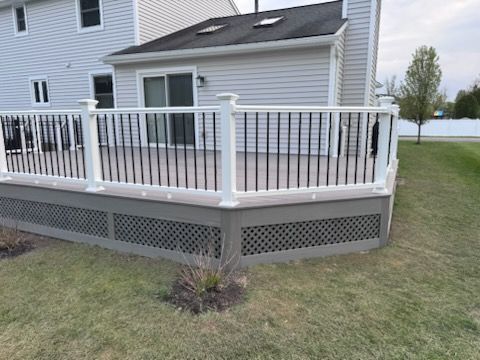 House deck with white railing and lattice skirting beside a grassy yard and lake view