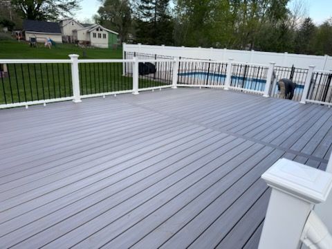 Gray composite deck with white railings overlooking a grassy yard and houses beyond