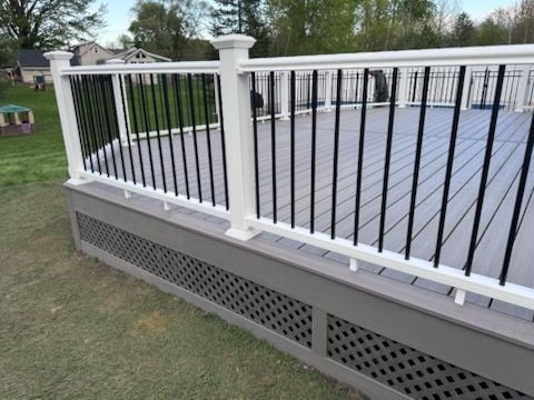 White and black deck railing on a raised outdoor platform beside a grassy yard.