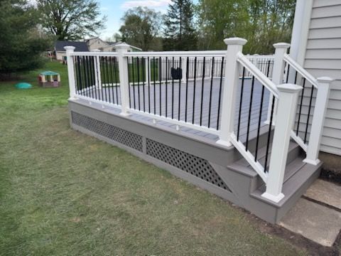 White deck railing and stairs on a gray porch beside a grassy backyard.
