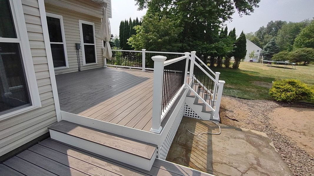White porch deck with steps and railing beside a house, leading to a gravel yard.