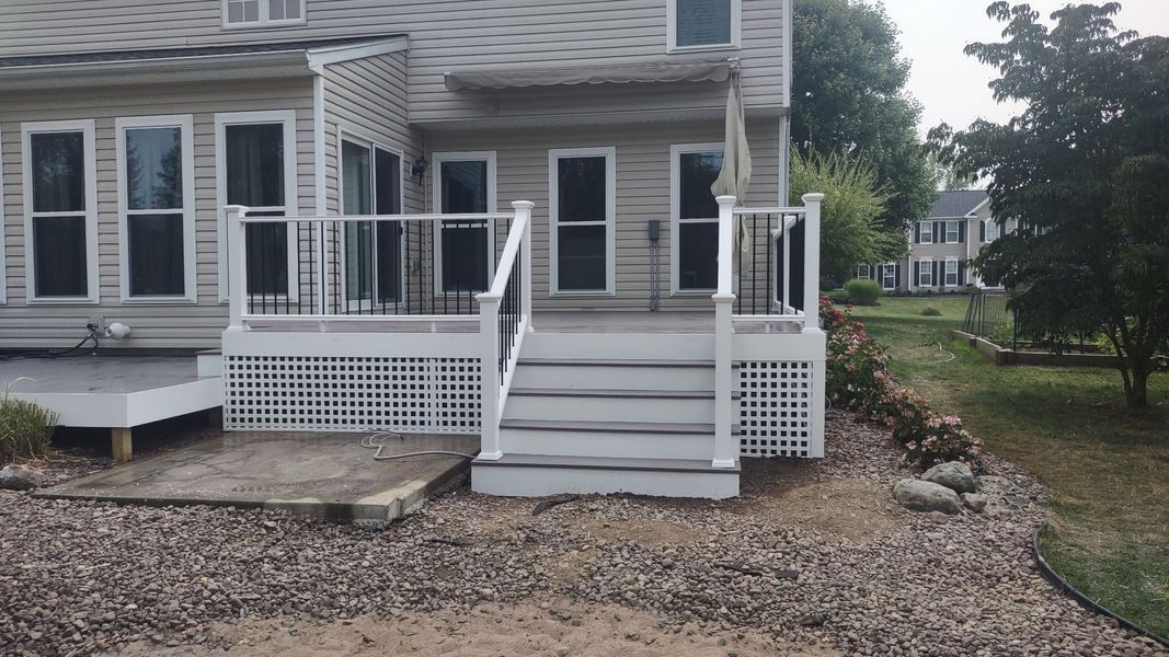 Front porch of a gray house with white railings, steps, and gravel landscaping around it