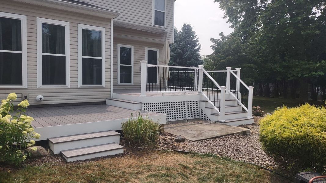 House exterior with a gray deck, white railings, and steps beside a stone walkway and shrubs