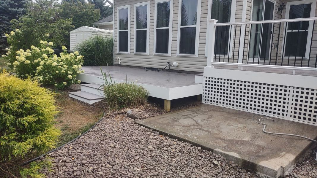 Small house porch with white lattice skirting, concrete patio, gravel path, and shrubs in a garden.