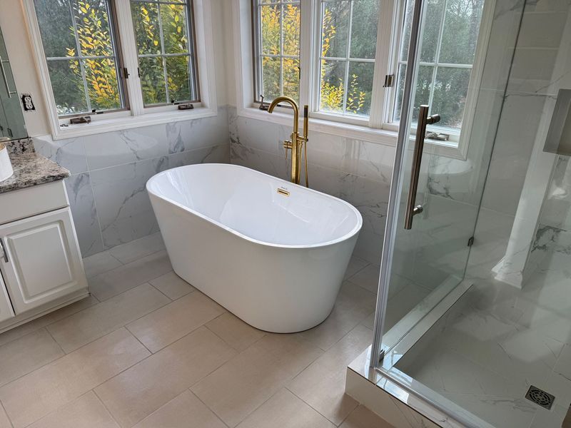 Bright modern bathroom with a white soaking tub, gold faucet, and glass shower