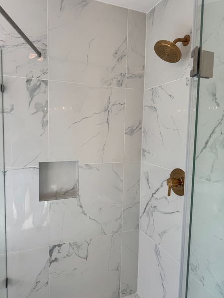 White marble-tile shower with brass fixtures and a built-in niche, seen through a glass door