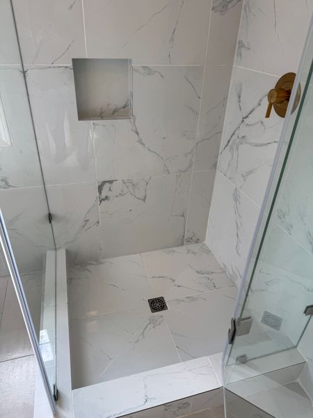 Empty tiled shower with glass door and built-in wall niche.