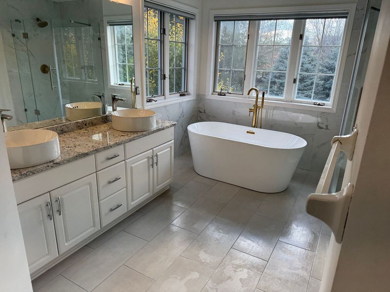 Bright modern bathroom with white freestanding tub, double vanity, and large windows.