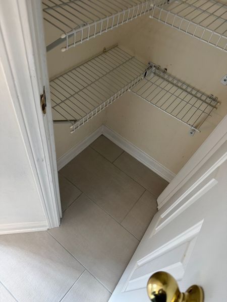 Empty walk-in closet with white wire shelves, beige walls, and tiled floor.