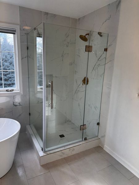 Modern bathroom with glass shower enclosure, white tub, and light tile floor