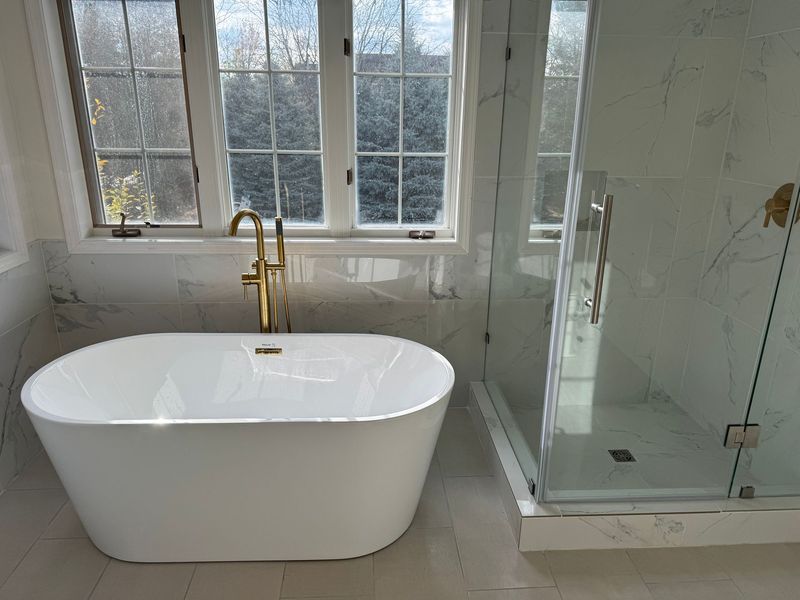 Modern bathroom with white bathtub, glass shower, and windowed wall