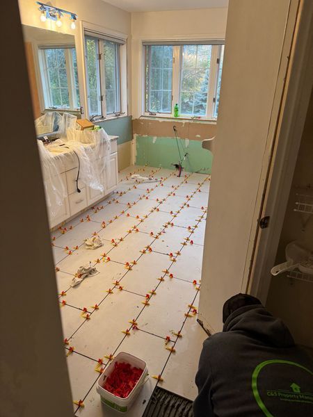 Bathroom under renovation with white floor tile, green lower walls, and a worker kneeling near the doorway.