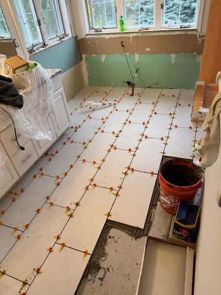 Kitchen floor being tiled in a room under renovation, with white tiles and exposed walls.