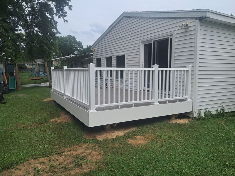 White-railed porch deck attached to a light gray mobile home in a grassy yard