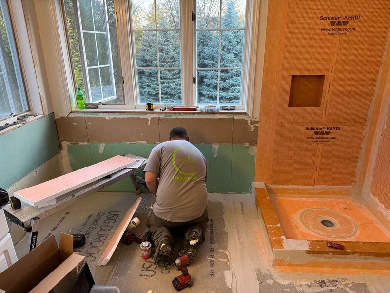 Worker installing bathroom wall insulation beside a window in a partially renovated room