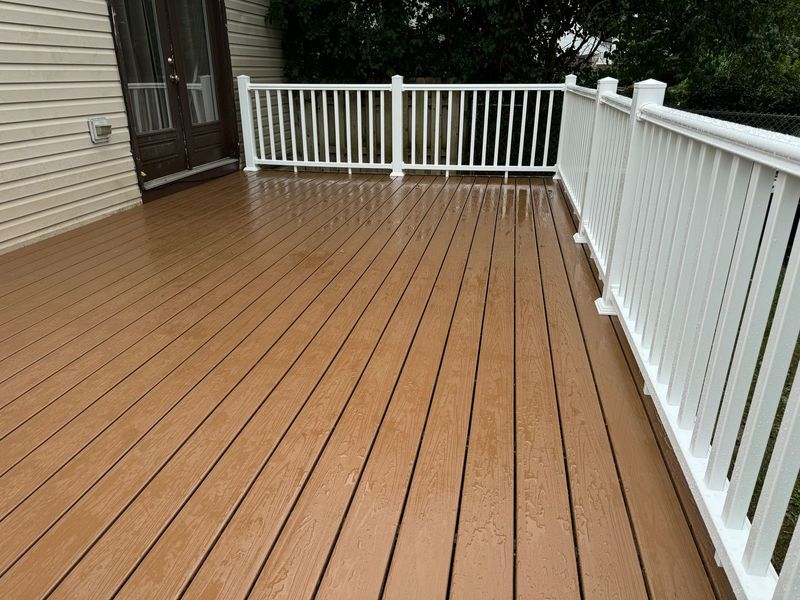 Empty wooden deck with white railing beside a house