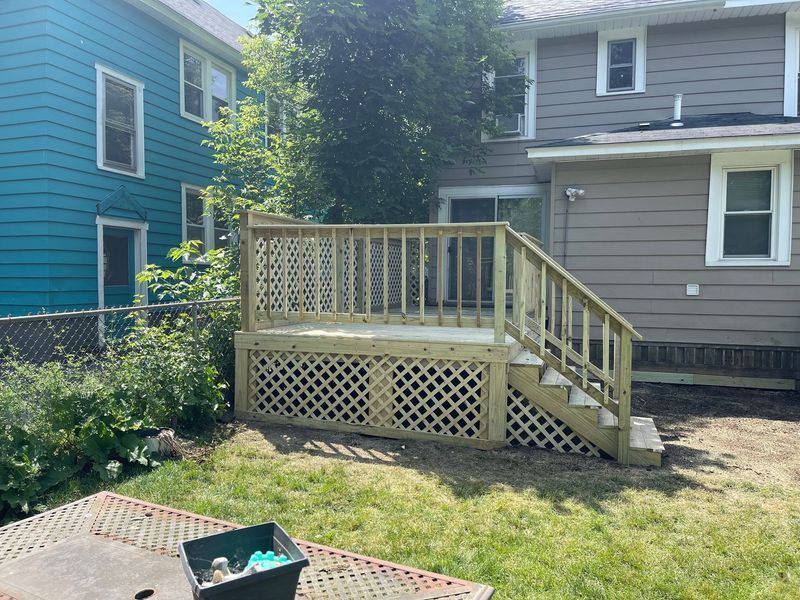 Backyard wooden deck with stairs and lattice, beside blue and gray houses