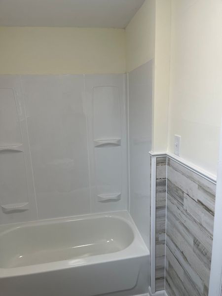 Bathtub and white shower surround in a bathroom with gray wood-look wall paneling