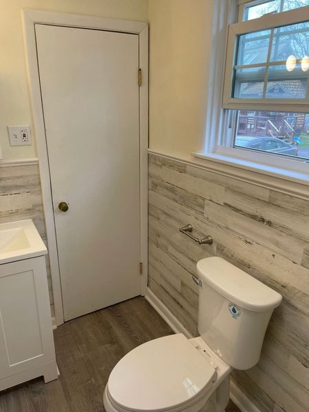 Small bathroom with a toilet, window, and white door beside a sink vanity.