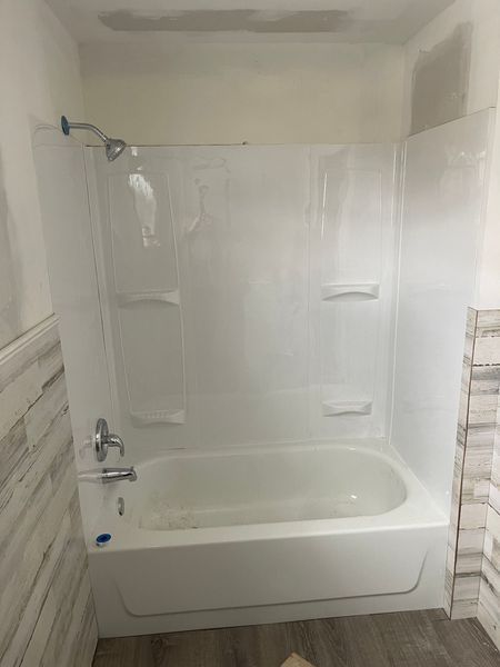 Bathroom with a white bathtub and shower enclosure against a tiled wall.