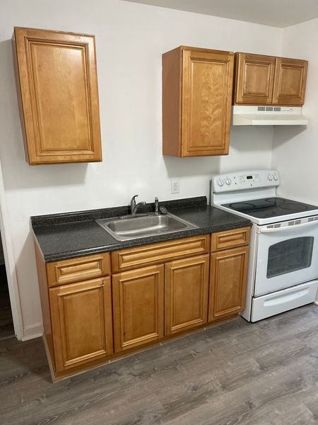 Small kitchen with wooden cabinets, black countertop, sink, stove, and gray flooring