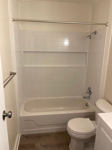 Small bathroom with white tub-shower, wall shelves, toilet, and sink vanity.
