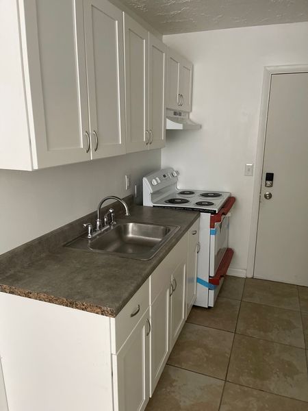 Small kitchen with white cabinets, sink, stove, and beige tile floor.