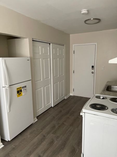 Small apartment kitchen with white fridge, stove, closet doors, and a back entry door on wood flooring