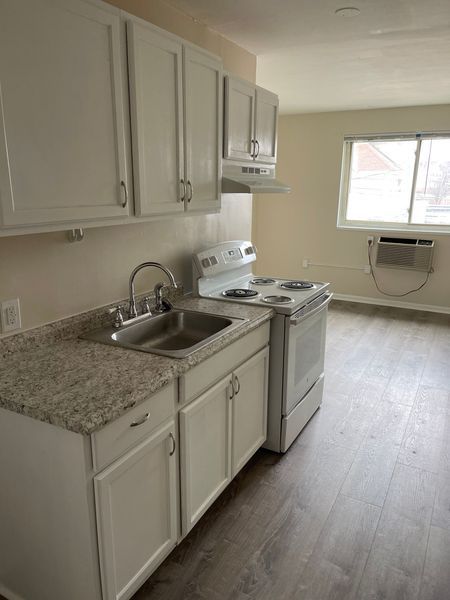Small kitchen with white cabinets, granite countertop, stove, sink, and a window air conditioner.