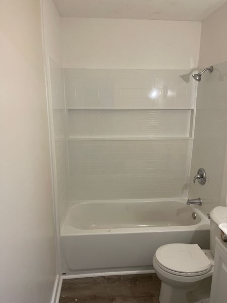 Small bathroom with a white tub-shower combo, built-in shelf, and a toilet in the foreground.