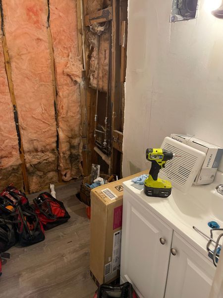 Laundry room with exposed insulation, a cordless drill on a washer, and tools on the floor