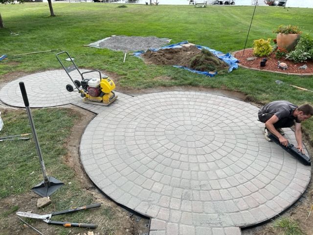 Worker smoothing a circular gray paver patio in a backyard garden