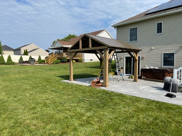 Backyard patio with wooden pergola, grill, and small fire pit beside a house on a grassy lawn
