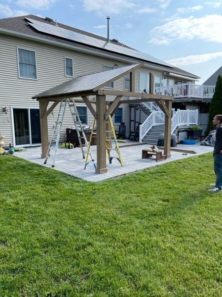 Backyard wooden pavilion with swings and a picnic table on a patio beside a house