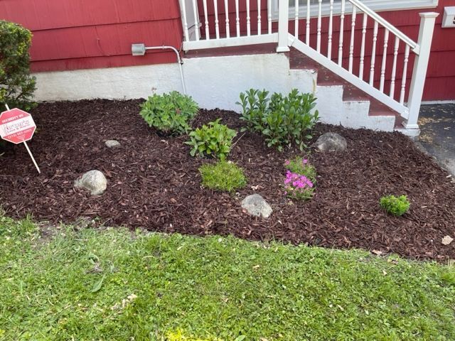 Small front yard flower bed with shrubs, mulch, and pink flowers beside red house steps
