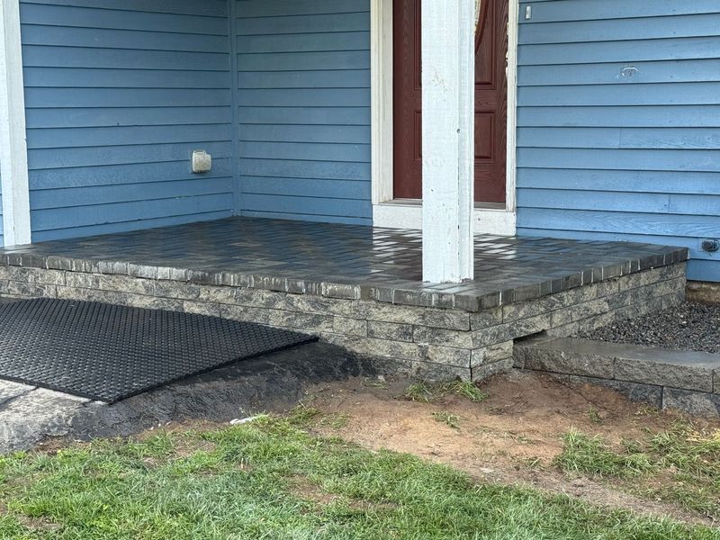 Front porch with blue siding, stone steps, and a black wheelchair ramp beside the entrance.