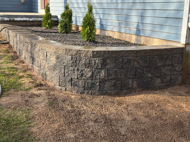 Stone retaining wall beside a house with small shrubs along the top edge