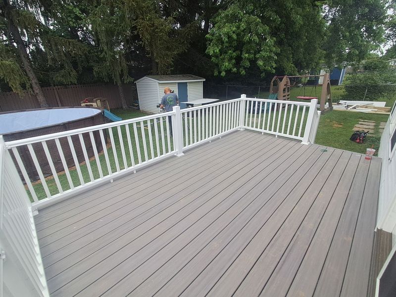 Raised gray deck with white railing overlooking a backyard with a pool and trees