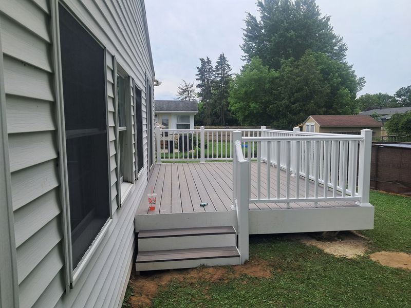 Back deck with gray steps, white railing, and sliding glass door beside a house