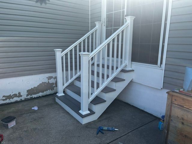 Small white porch stairs with railing beside a house, showing uneven paving and a blue tool on the ground.